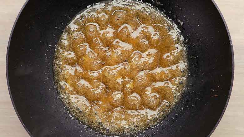 A close up shot of honey sauce being cooked and thickened in a black wok – Honey Chicken Recipe