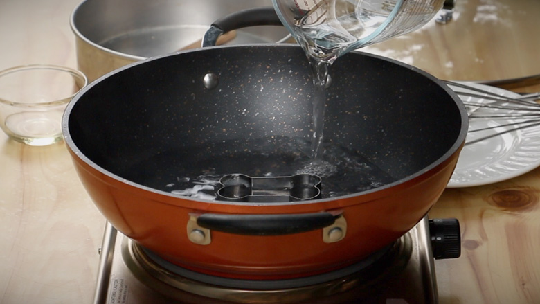 Prepare your homemade steamer by placing a small metal bowl or cookie mould at the bottom of a kadhai / wok and adding water - Khaman Dhokla Recipe