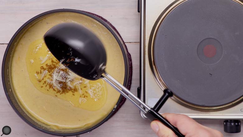 Pour the tempering of ghee, garlic, and cumin seeds over the sultani dal and stir through - Awadhi Style Dal Sultani Recipe