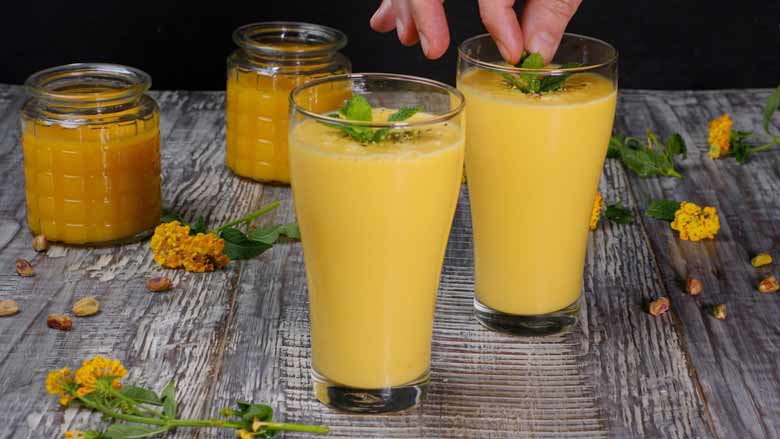 Pour mango lassi into tall glasses, sprinkle with finely chopped pista, and top with a sprig of mint each - Mango Lassi Recipe