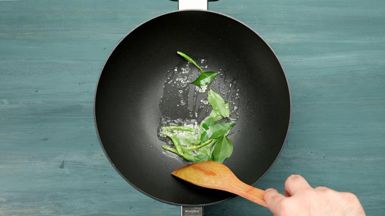 Heat oil in a kadhai and toss in green chillies, garlic, and curry leaves - Potato 65 Recipe