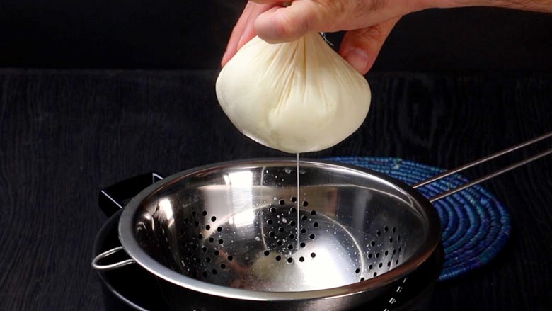 Pick up the corners of the cheese cloth or muslin cloth and twist and tighten gently, forming a tight pouch to remove liquid whey from the paneer - How to make paneer from milk at home
