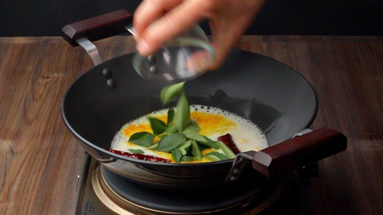 Frying curry leaves in sesame oil in a kadhai along with whole spices and seeds for the Tamarind Rice sauce