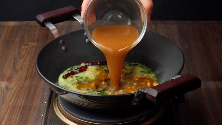 Pouring prepared tamarind water into the masala mixture of curry leaves, whole spices, and seeds for Tamarind Rice
