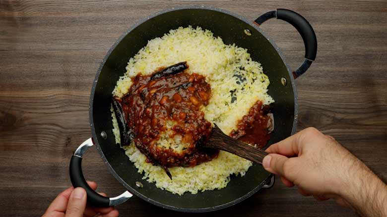 Gently mixing tamarind sauce with the cooked rice in the kadhai using a wooden spatula for Tamarind Rice