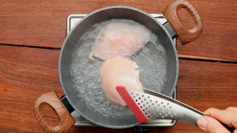 Placing one boneless chicken breast and thigh in boiling water in a medium saucepan with wooden handles for the best chicken salad recipe