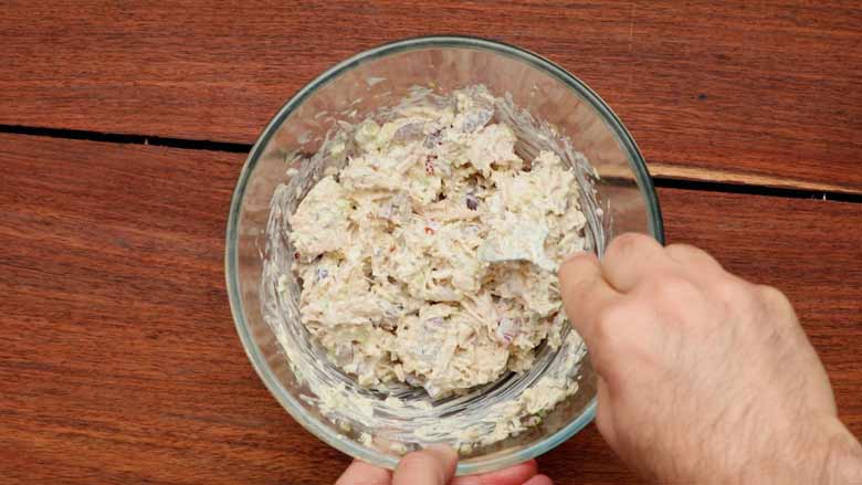 Mixing together the mayonnaise and all other ingredients of the chicken salad in a glass bowl with a spoon to combine well before chilling in the refrigerator