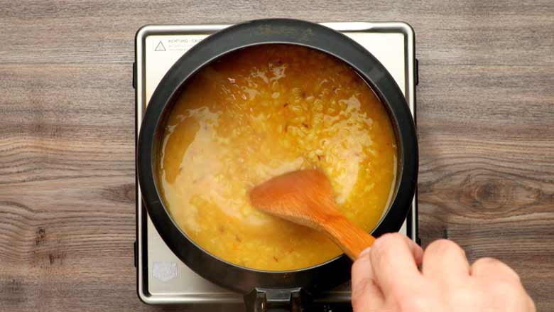 Cooked dal being stirred with a wooden spatula in a black pressure cooker opened after cooking
