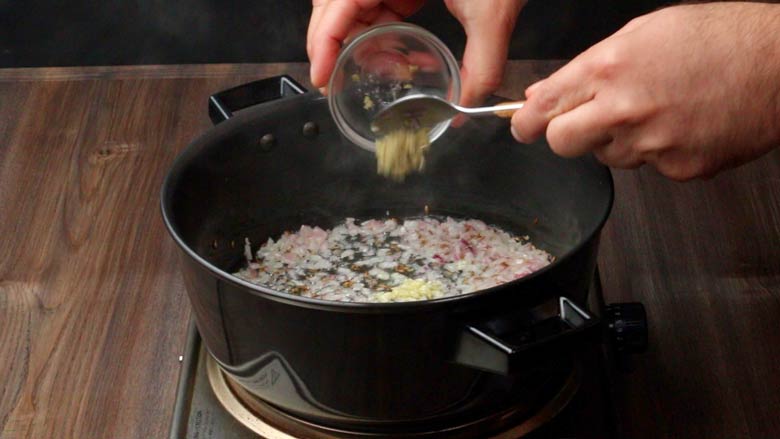 Adding ginger and garlic to onions being fried in a black pan preparing the tadka for dal tadka