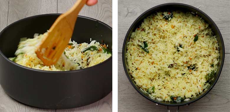 The tempering of spices, dals, and curry leaves being gently mixed with a wooden spatula into the boiled rice in a black pan on a white textured wooden table to make Lemon Rice