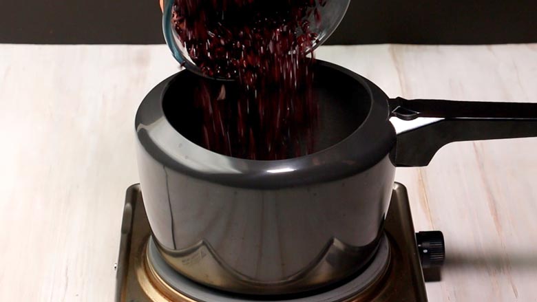 Soaked black rice in a glass bowl being tipped into a black pressure cooker to make kavanarisi