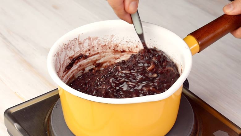 Stirring kavanarisi with a spoon till ready in a yellow and white saucepan with a wooden handle on an electric stove on a white textured table