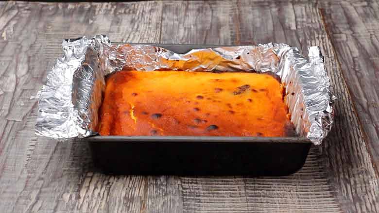 Golden brown Cheesecake Brownies freshly baked and out of the oven in a baking tin lined with foil on a white and grey textured wooden table