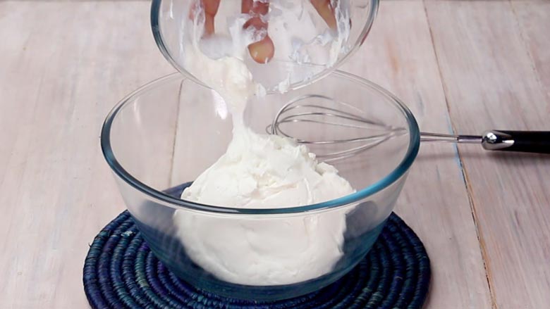 Hung yogurt or curd called chakka being tipped into a glass bowl lying on as blue coiled mat on a textured white wooden table for kesar shrikhand