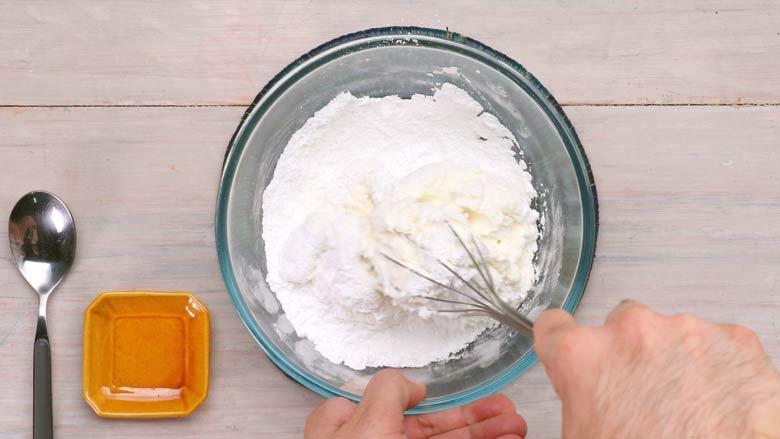 Sugar being whisked into the hung yogurt in a glass bowl with a balloon whisk for Saffron Shrikhand