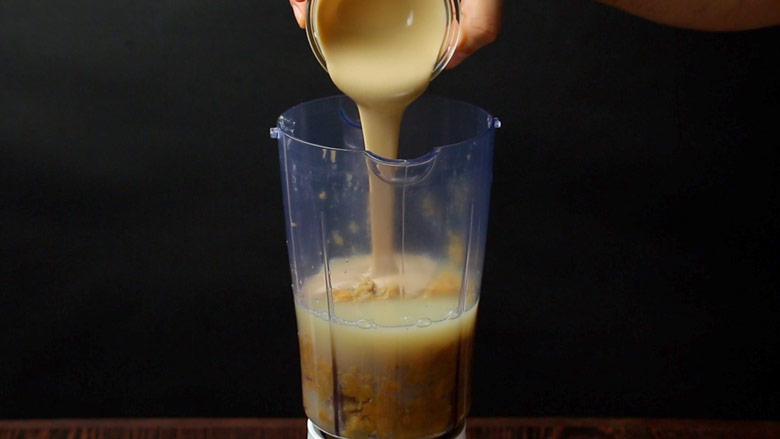Tahini being poured into a blender containing cooked chickpeas and lemon juice for hummus