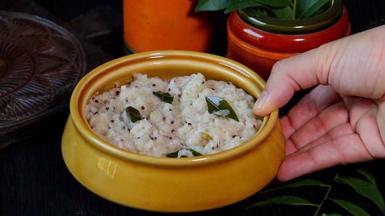 A hand serving Rice Upma in a ochre ceramic dish with a lacquered brick-coloured bowl in the background - Rice Upma Arisi Upma Recipe