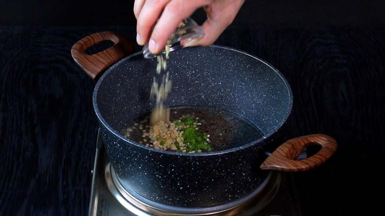 Tempering of ginger, green chillies, and black mustard seeds being prepared in a grey and white speckled pan with wooden handles for rice upma
