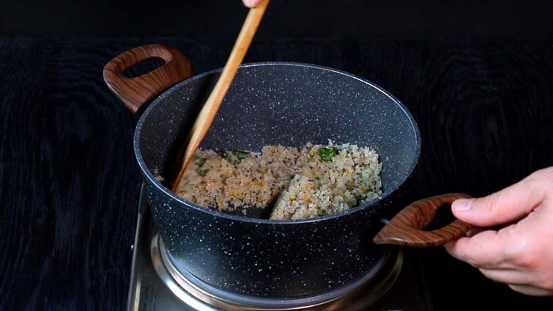 A wooden spatula stirring the rice upma mixture to roast the ground rice in a grey and white speckled pan with wooden handles for rice upma