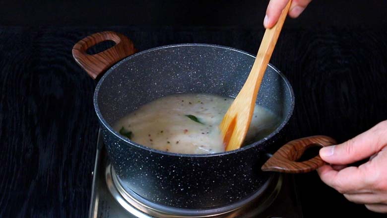 A wooden spatula stirring the rice upma mixture after water has been added to the pan - Rice Upma Arisi Upma Recipe