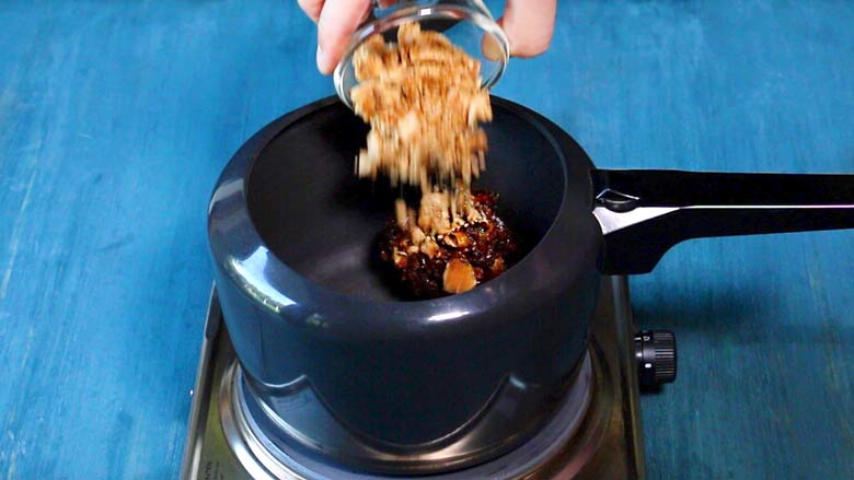 Jaggery being added to chopped dates in a black pressure cooker on a metallic electric stove lying on a blue table - Sweet Chutney Recipe