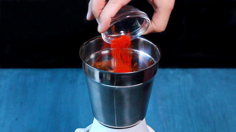 Red chilli powder being added to a tabletop metallic grinder to make Date and Tamarind Chutney - Sweet Chutney Recipe