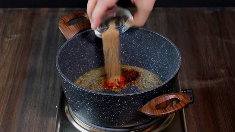 Spices being aded to a black and white speckled pan with wooden handles on a stove to prepare Dry Brown Chana Masala - Sukha Brown Chana Masala Recipe