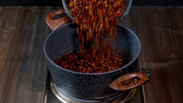 Adding cooked kala chana to the cooked masala in a speckled black and white pan with wooden handles on a metallic stove - Dry Brown Chana Masala Recipe