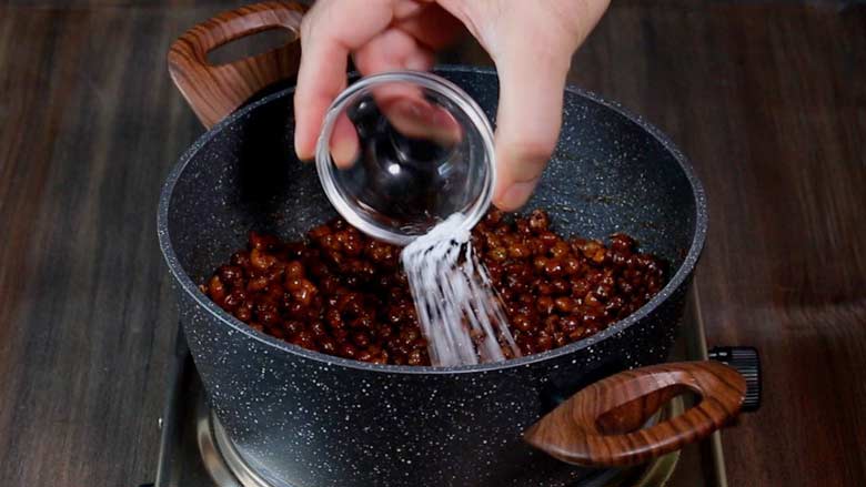 Adding Navratri approved sendha namak to sukha kala chana masala cooking in a black and white pan on a stove on a wooden counter - Dry Brown Chana masala Recipe