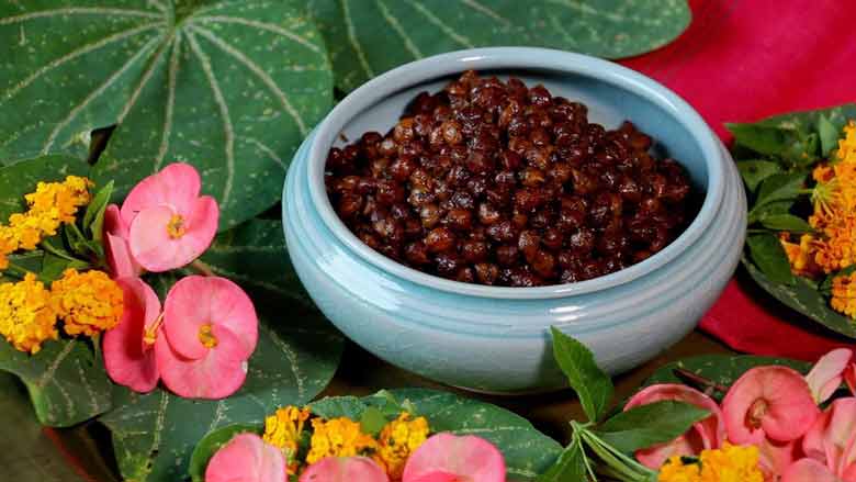 A closer shot of Sukha Kala Chana Masala in an aqua ceramic bowl surrounded by Indian Orchid leaves and peach, pink, and orange coloured flowers, and a red fabric - Sukha Kala Chana Masala Recipe