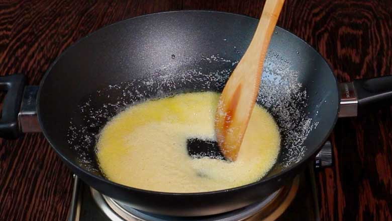 A wooden spatula stirring semolina or suji or rava in ghee in a large black kadhai while preparing suji ka halwa - Suji Halwa recipe