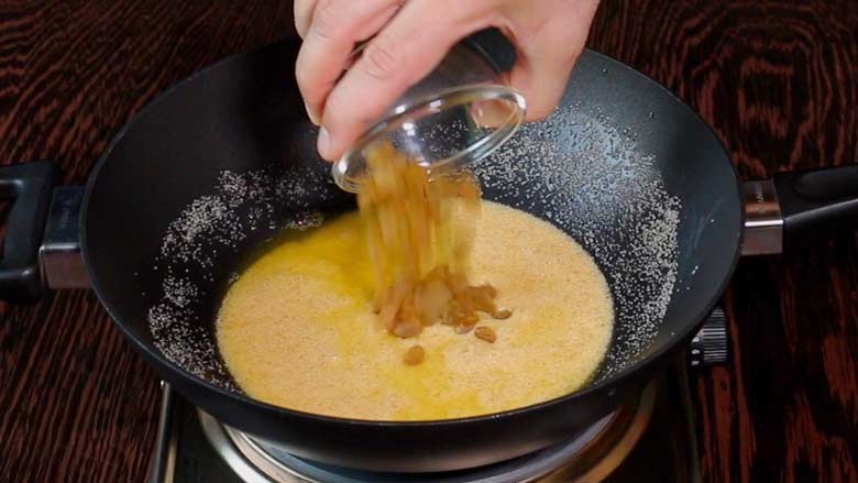 Raisins or kishmish being added to the lightly browned suji - semolina - in ghee in a large black one-handled kadhai over an electric stove - Suji Halwa recipe