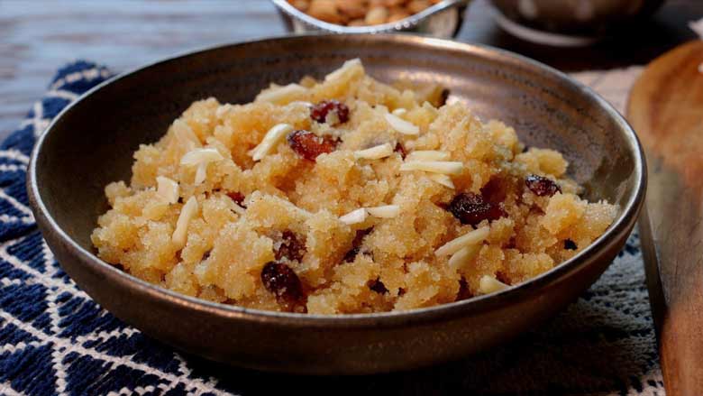 Rava sheera (suji ka halwa) garnished with almonds in a bronze coloured ceramic bowl on a blue and white woven fabric mat. Ready to eat - Suji Halwa recipe