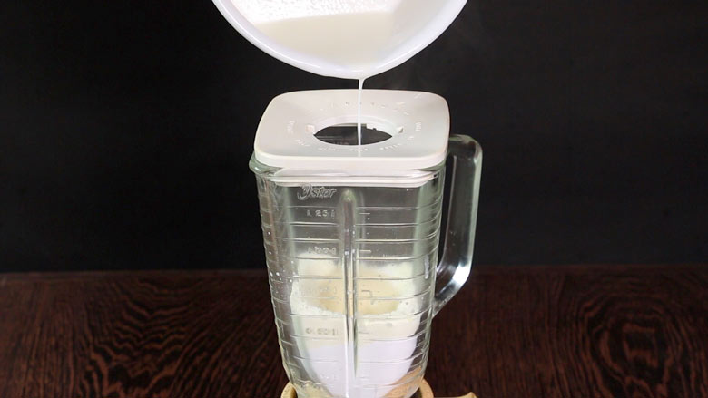 Hot milk being poured into a running blender through the hole in the lid from a white saucepan - Homemade Condensed Milk Recipe