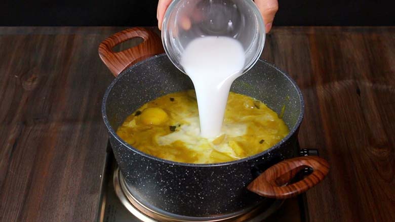 Pouring thick coconut milk into the cooked potato curry Kerala Style in a black and white speckled pan with wooden handles to finish cooking the Potato Mappas