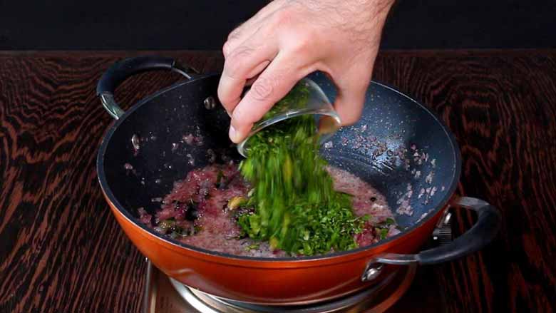 Fresh coriander leaves being tipped from a small glass bowl into an orange non stick pan with onions already cooked till translucent in the pan - Keema Curry Recipe Konkani Style