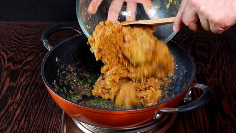Marinated minced meat being added to an orange non-stick pan from a glass bowl with a wooden spatula - Keema Curry recipe Konkani Style
