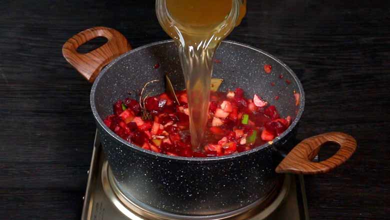 Veg stock is poured into a non stick pan with diced beetroot and other vegetables and spices cooking in it to make borscht - Borscht Soup Recipe