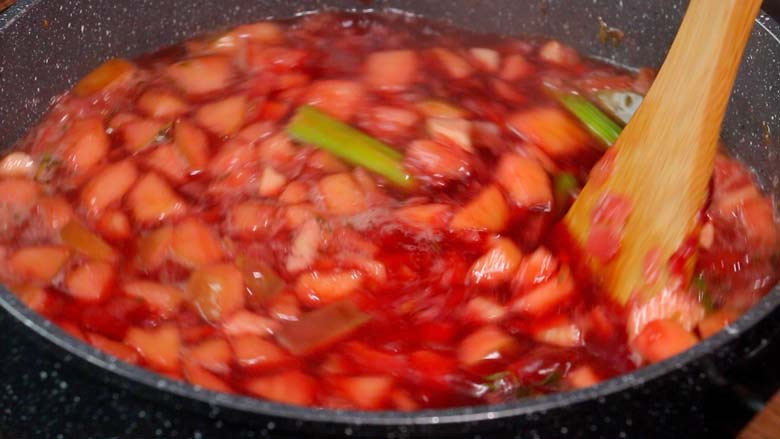 A close up side shot of borscht soup being cooked and stirred with a wooden spatula - Borscht Soup Recipe