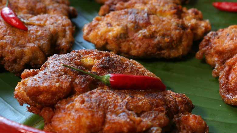 A closeup shot of Parsi style Crispy fried chicken pieces garnished with red whole chillies lying on a banana leaf in a Burmese lacquer platter - Chicken Farcha Recipe