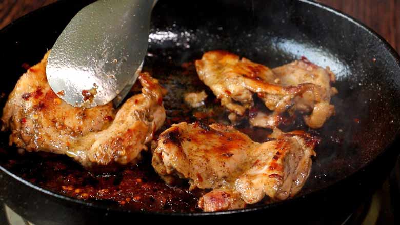 Tongs are seen turning a nicely grilled piece of chicken in a heavy black cast iron frying pan with two other pieces of chicken also grilling in the pan - Chicken Shawarma Recipe
