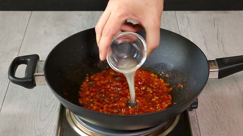  Lime juice is poured out from a glass bowl into a black kadhai with the chilli sauce after the heat is turned off - Chilli Potato Salad Recipe
