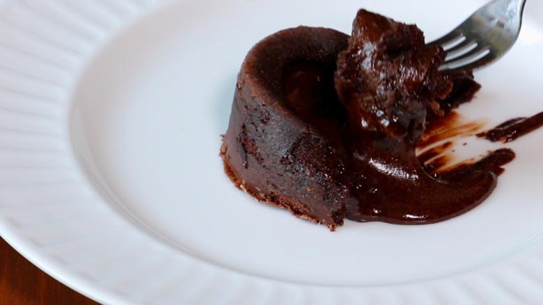 A closeup shot of a fork lifting off cake and oozing chocolate from a white plate for a large bite - Chocolate Lava Cake Recipe