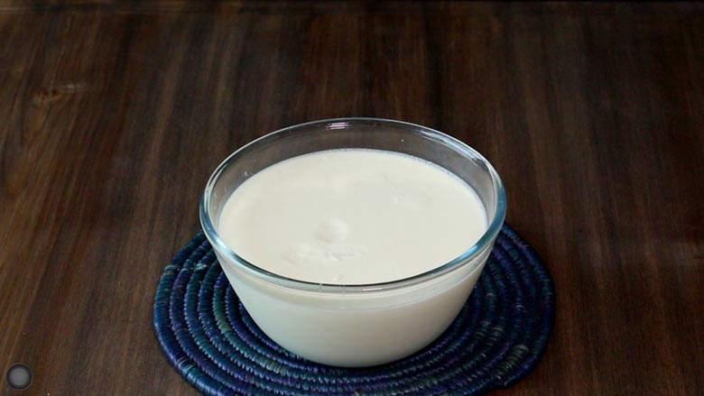 Yogurt that has been set in a glass bowl lying on a blue cane mat on a dark wooden counter top - Homemade Yogurt Recipe