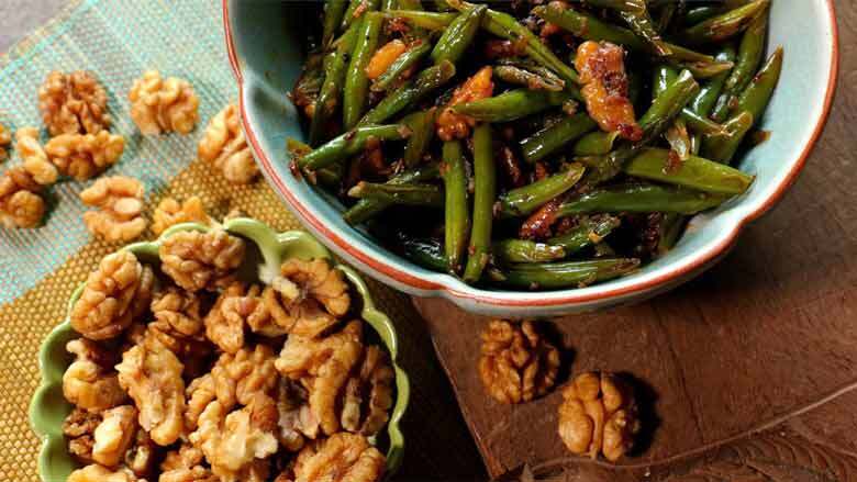 A top shot of Indian green beans and walnuts in a blue celadon ceramic bowl next to a green bowl full of California walnut kernels - Indian Green Beans with Walnuts Recipe Caption: Spicy green beans cooked with California walnuts