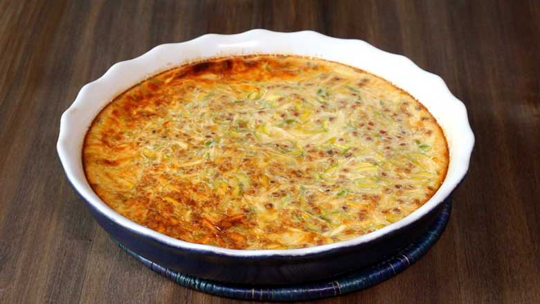 A nicely caramelised Parsi baked custard in a white and blue ceramic baking dish lies on a blue cane mat on a dark wooden table - Lagan Nu Custard Recipe