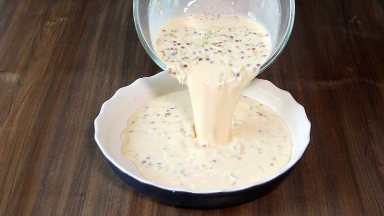 The egg custard mixture is being poured into white and blue fluted pie dish made of ceramic on a dark wooden countertop - Lagan Nu Custard Recipe