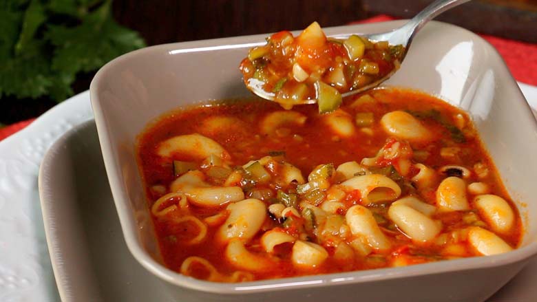 Minestrone soup is seen being eaten with a spoon from the grey square bowl with curved corners - Minestrone Soup Recipe