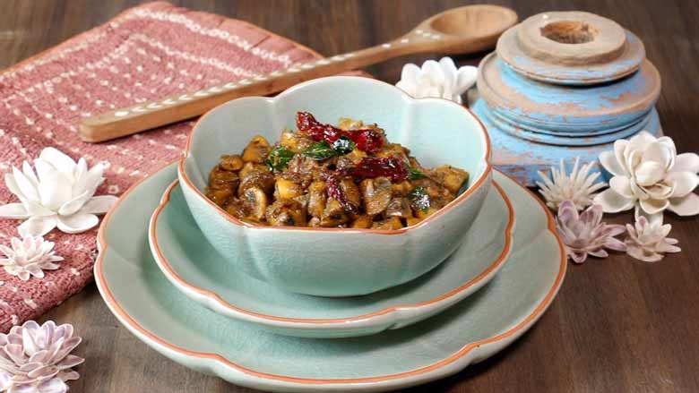 A side image of mushroom pepper fry in a teal ceramic bowl with a terracotta coloured rim on two plates of the same colour. A copper-clay colour tie-dye fabric, shell flowers, inlaid wooden spoon, and a blue wooden piece lie in the background - Mushroom Pepper fry Recipe