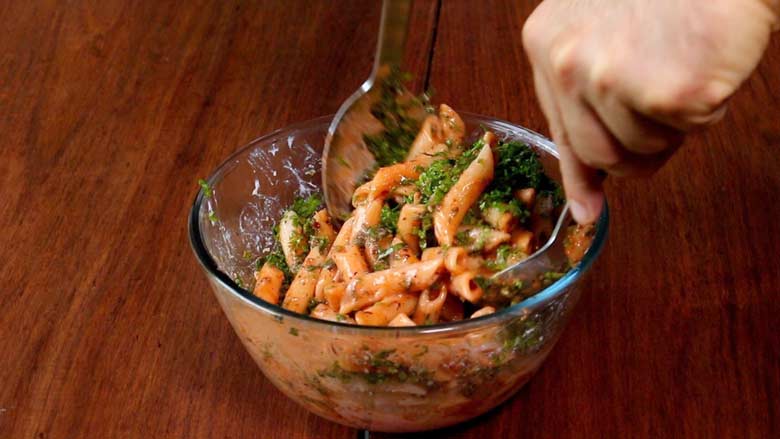 Two large spoons are being used to toss penne pasta with its sauces and herbs in a glass bowl - Pasta with Herb Butter Sauce Recipe